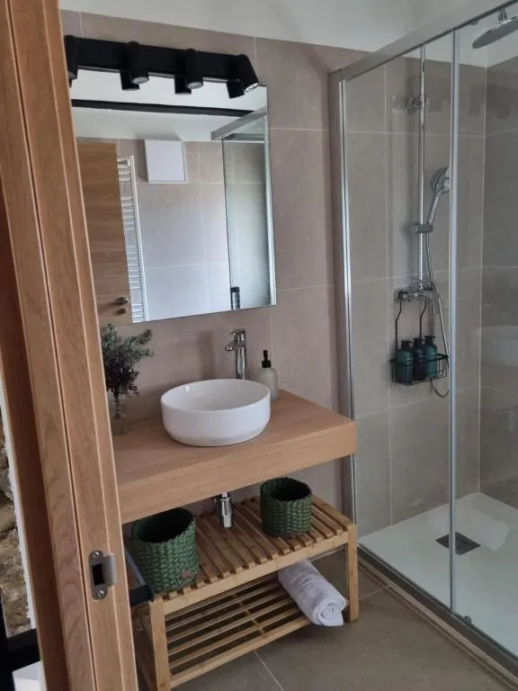 White basin on a wooden vanity unit with wicker baskets and a glass shower alongside