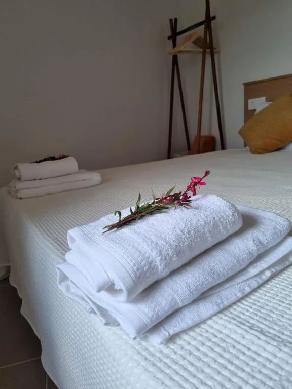 White towels folded on the bed with a pink welcome flower