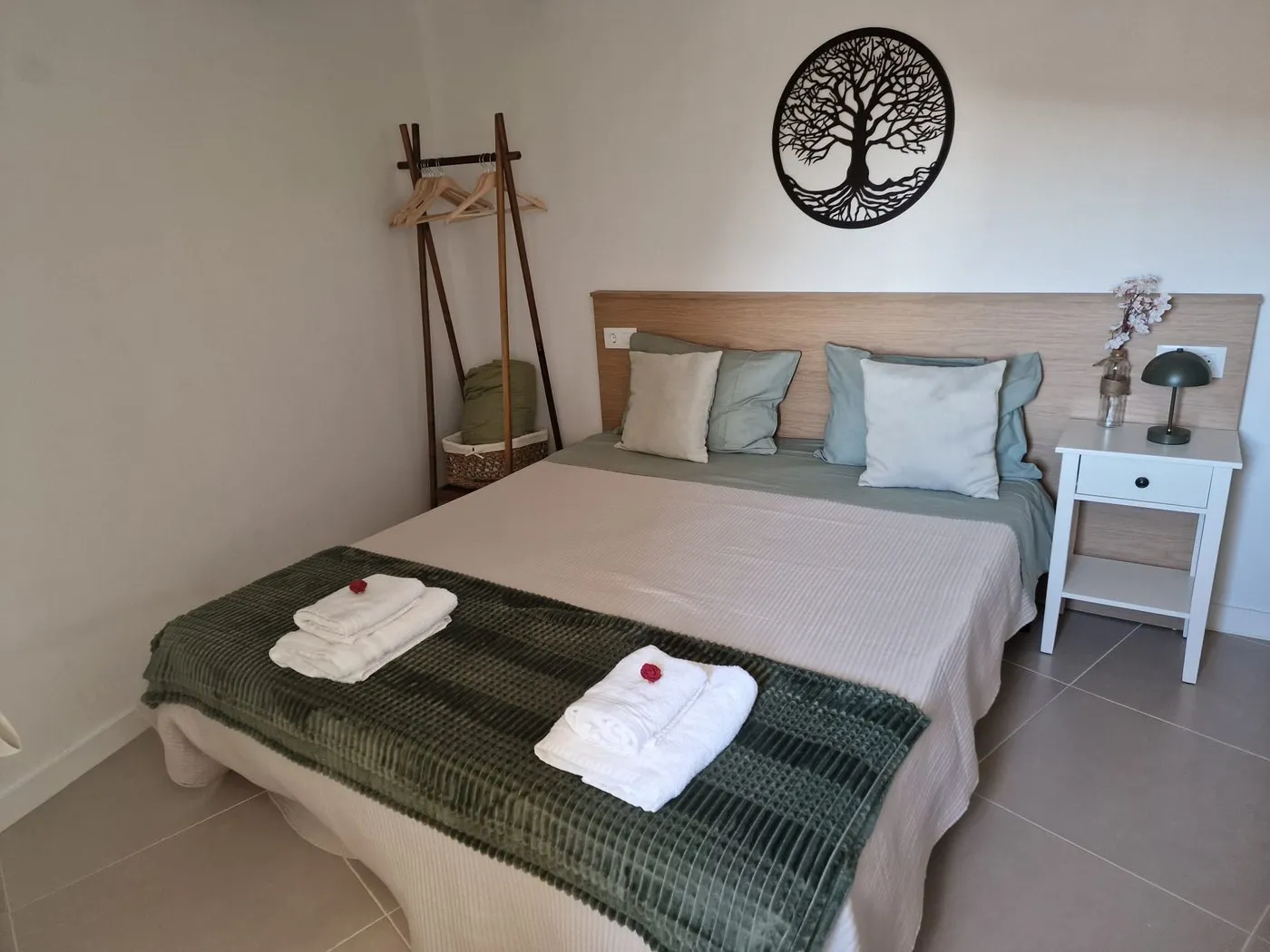 Double bedroom with the bed made up, rolled towels with a rose on top and a wrought-iron tree of life on the wall
