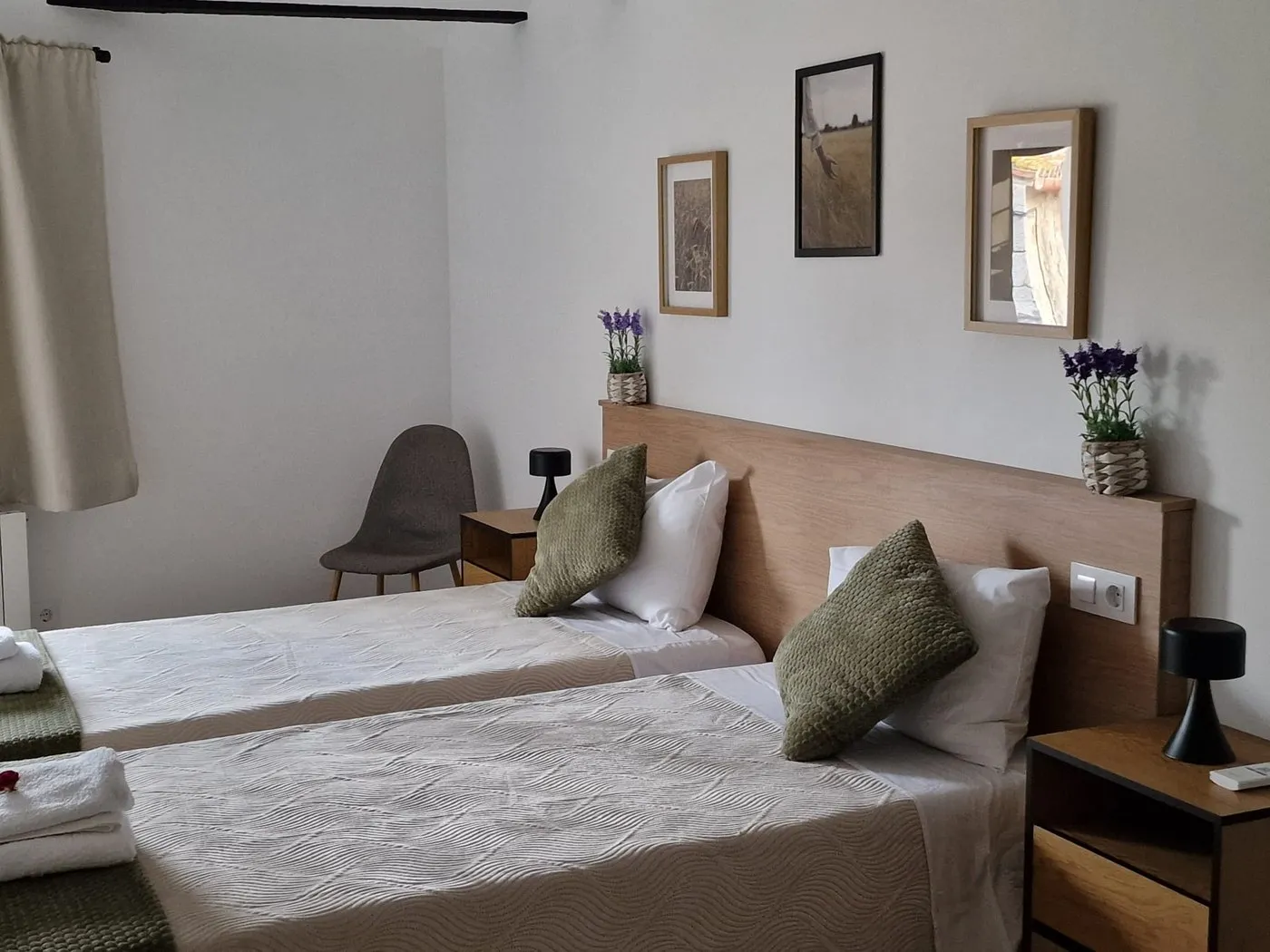 Bedroom with two single beds pushed together, olive-green velvet cushions and framed prints above the wooden headboard