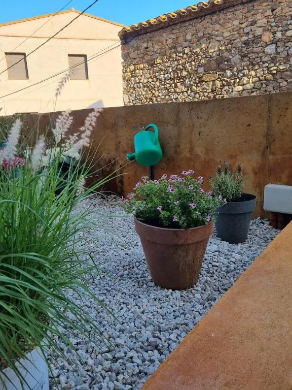 Terracotta pots with flowers on the gravel, in front of the stone wall and the hanging watering can