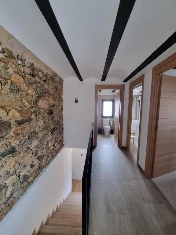 Upper-floor corridor with a dry-stone wall and black steel beams in the ceiling